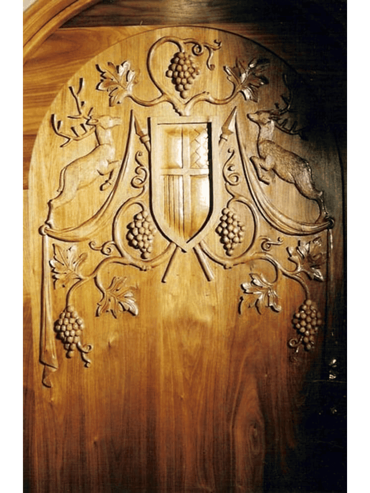Hand-carved solid wood wine cellar door featuring deep-relief vineyard crest, grape vines, and rich natural wood tones