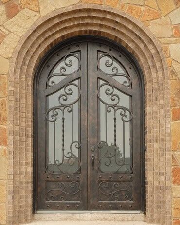 Vintage arched double wrought iron door EL1128 MCD with ornate scrollwork, tall glass panels, and decorative lower panels.