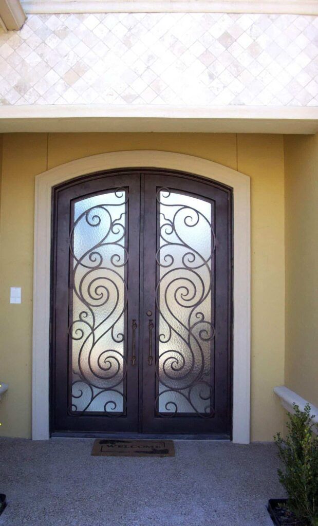 Arched wrought iron door EL1113 MCD with flowing scrollwork and frosted glass, hand-forged for elegance and privacy.